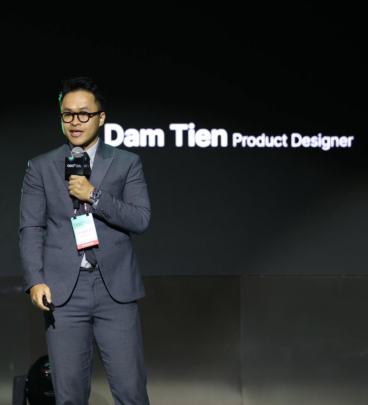 Dam Tien speaking on stage with a microphone, his name and 'Product Designer' on the screen behind him