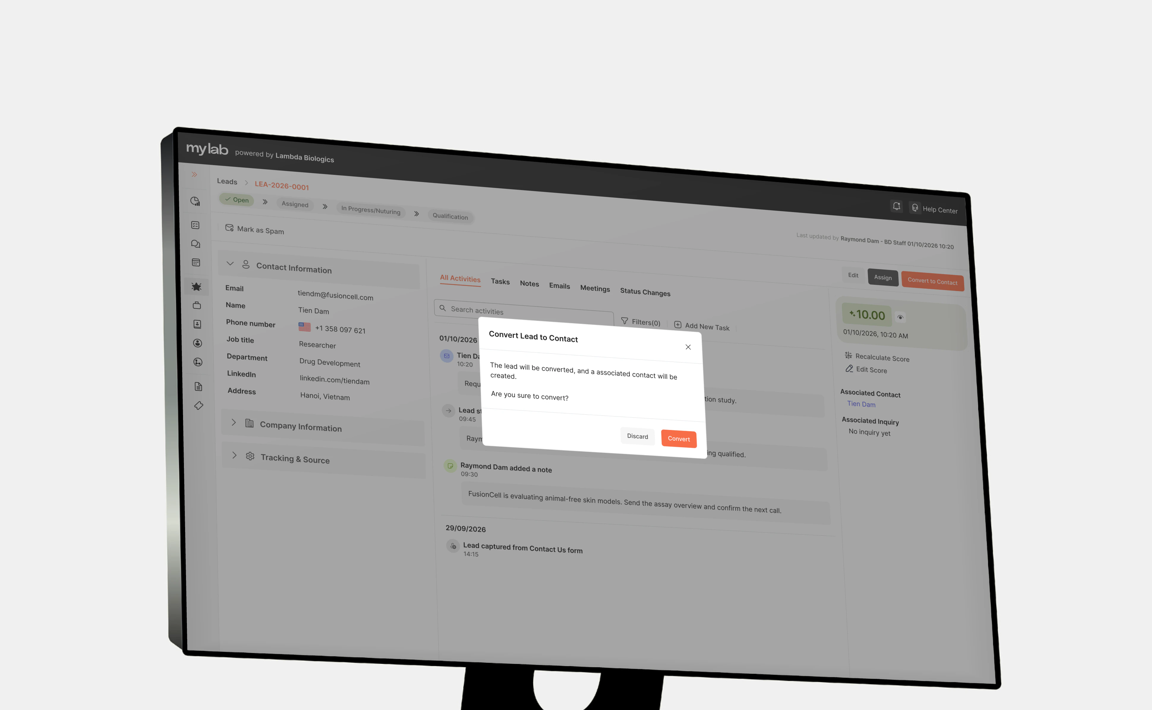 A MyLab CRM lead detail page on an angled monitor, dimmed behind a Convert Lead to Contact dialog that explains the lead will be converted and an associated contact created, with Discard and Convert buttons