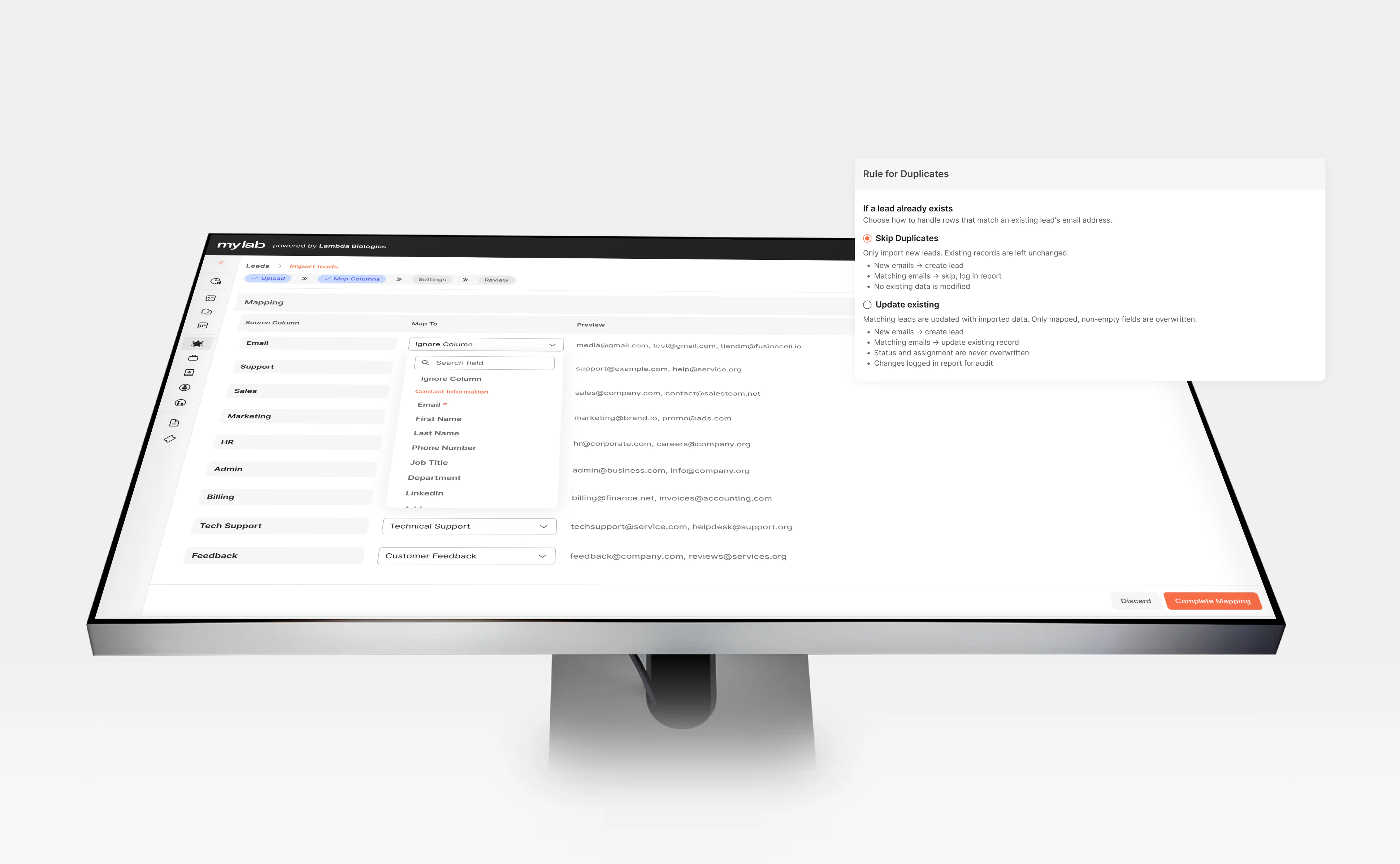 The MyLab CRM Import leads screen on a monitor seen from above, at the Map Columns step: source columns such as Email, Support and Sales mapped to CRM fields, with a field picker open on Contact Information - and a Rule for Duplicates panel beside it, choosing between Skip Duplicates and Update existing when a lead's email already exists