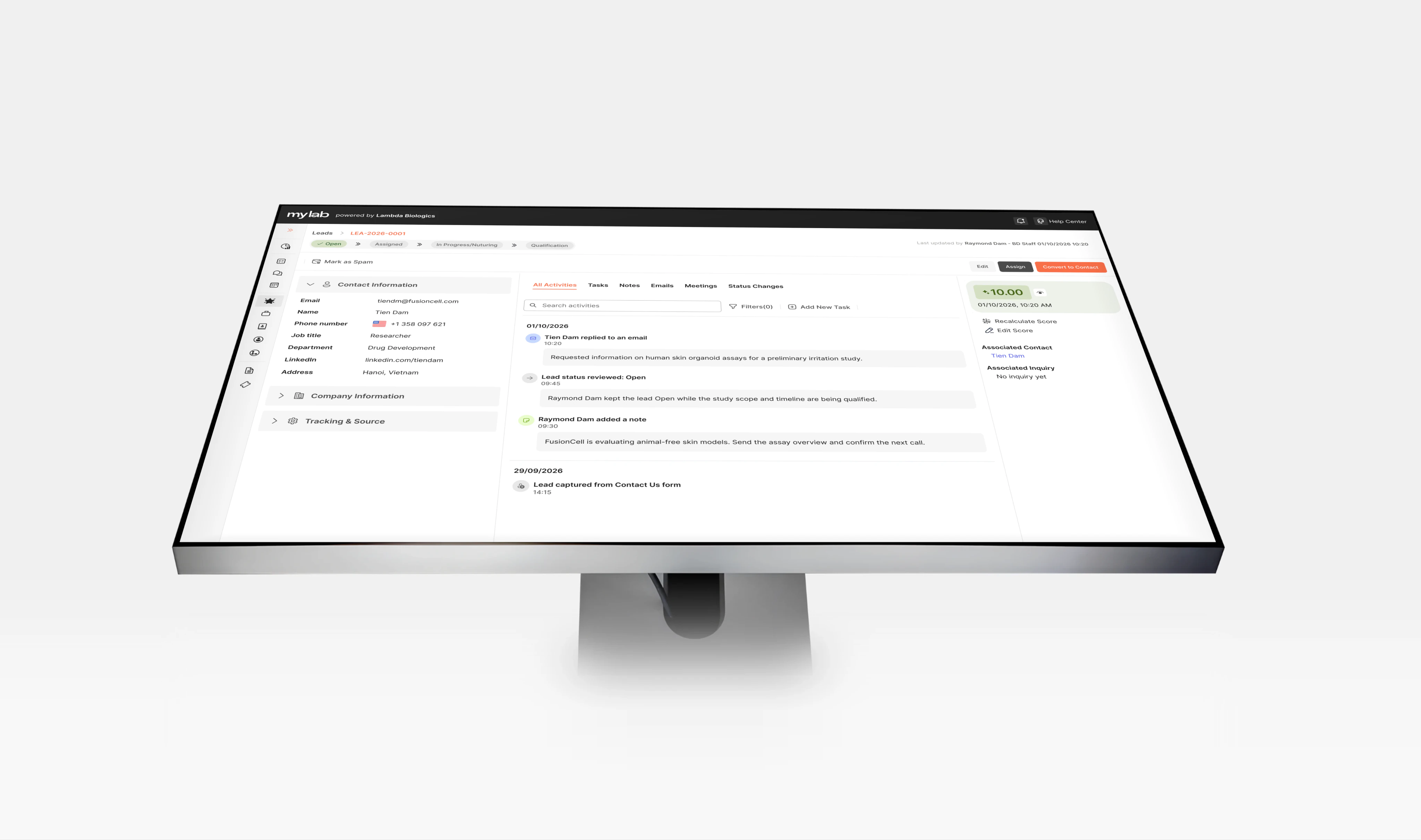 A MyLab CRM lead detail page on a large monitor seen from above, against a pale grey background: the lead's status steps, contact information, an activity timeline of emails, notes and status changes, and the lead score